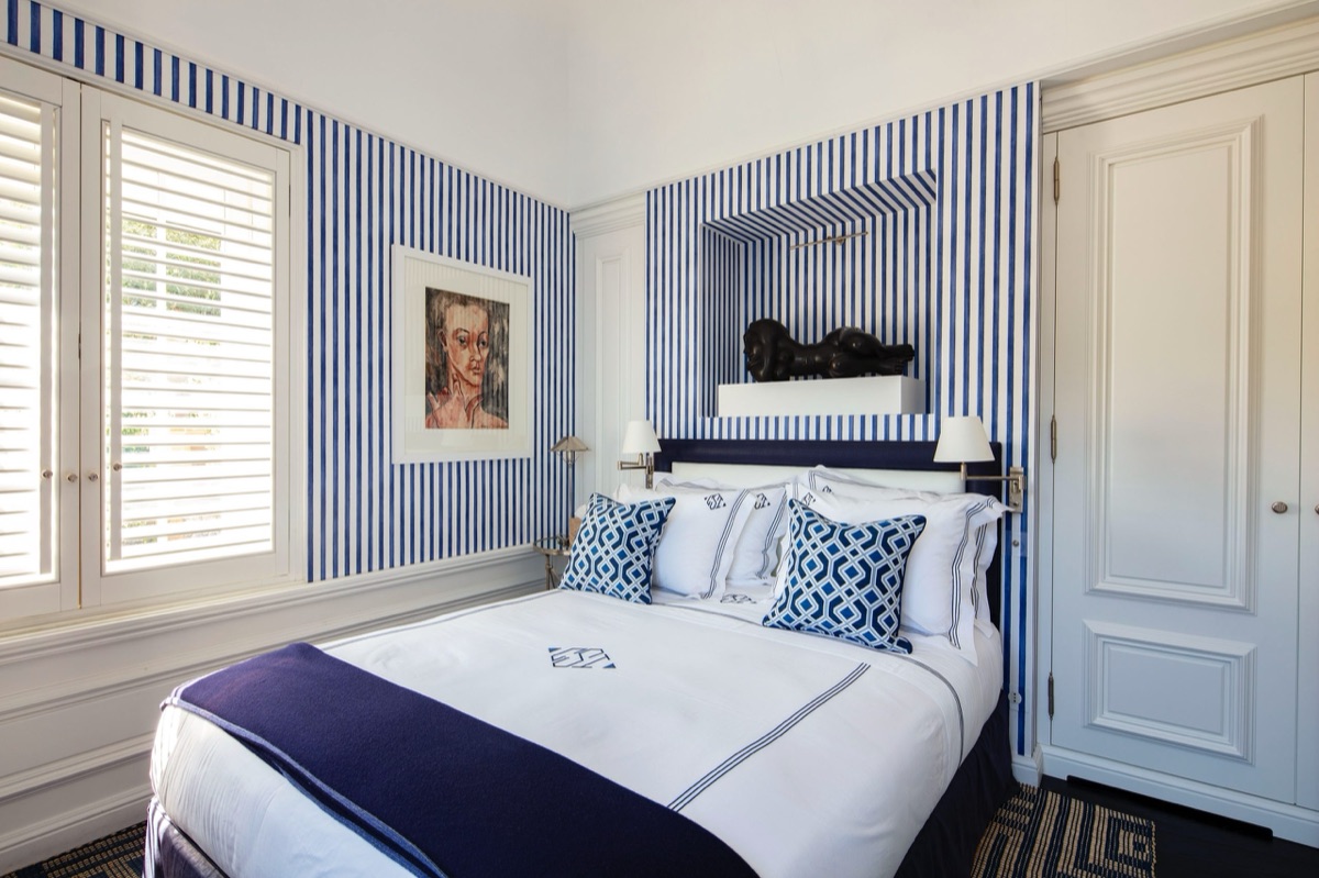 A bedroom papered in blue and white stripes, the bed dressed to match