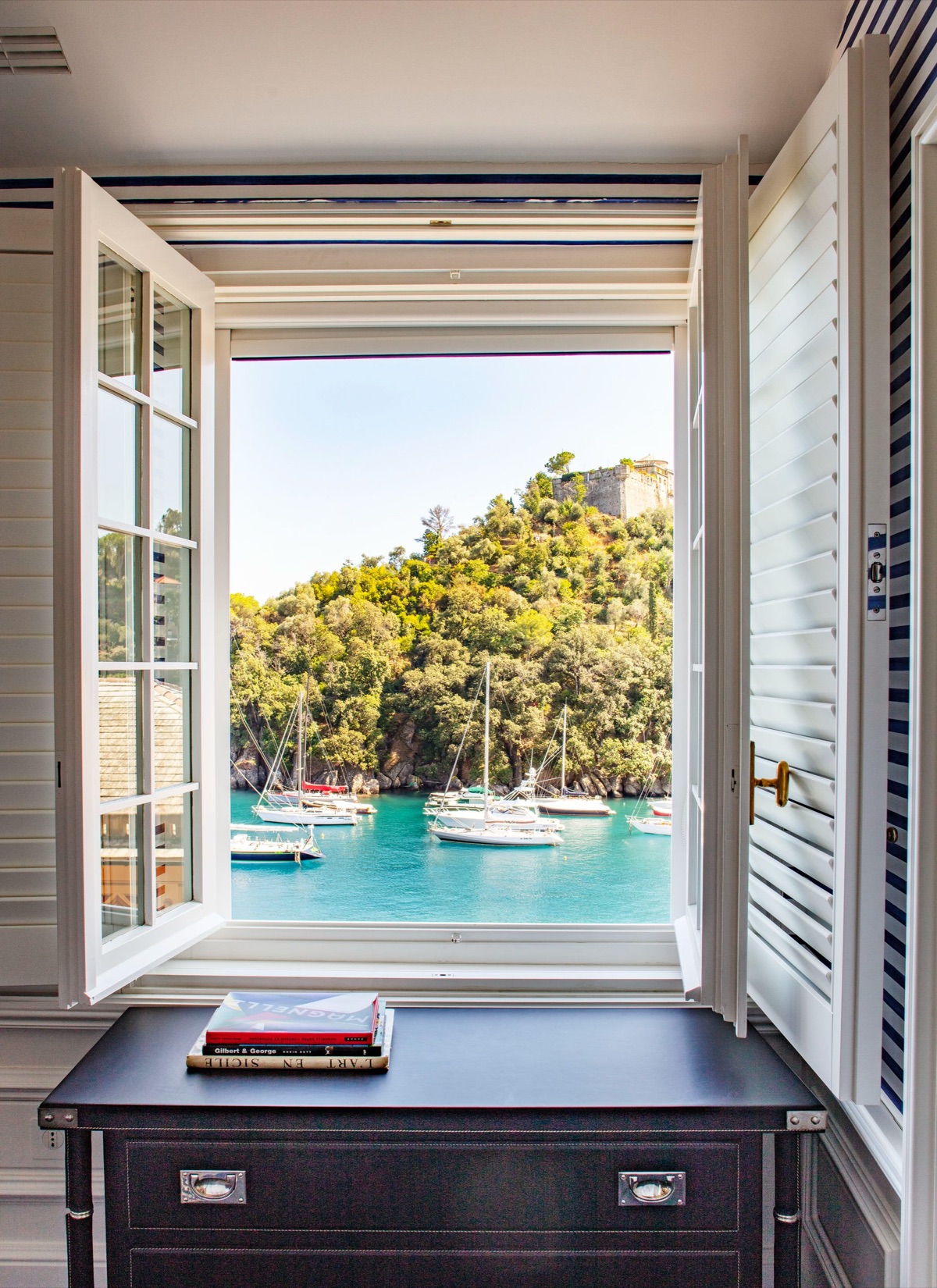 Shutters thrown open on a Mediterranean harbour, the boats at anchor below