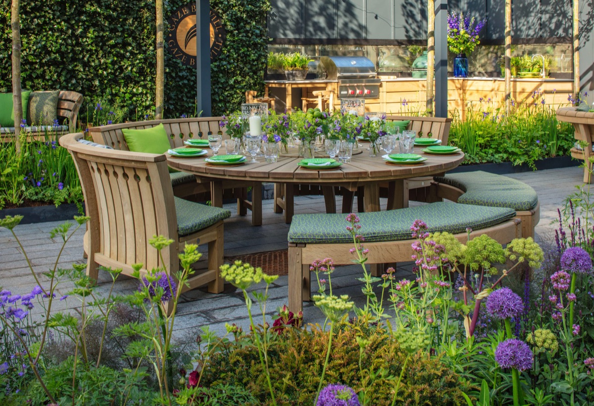 A round Gaze Burvill oak table laid for dinner, candles lit, in a planted courtyard